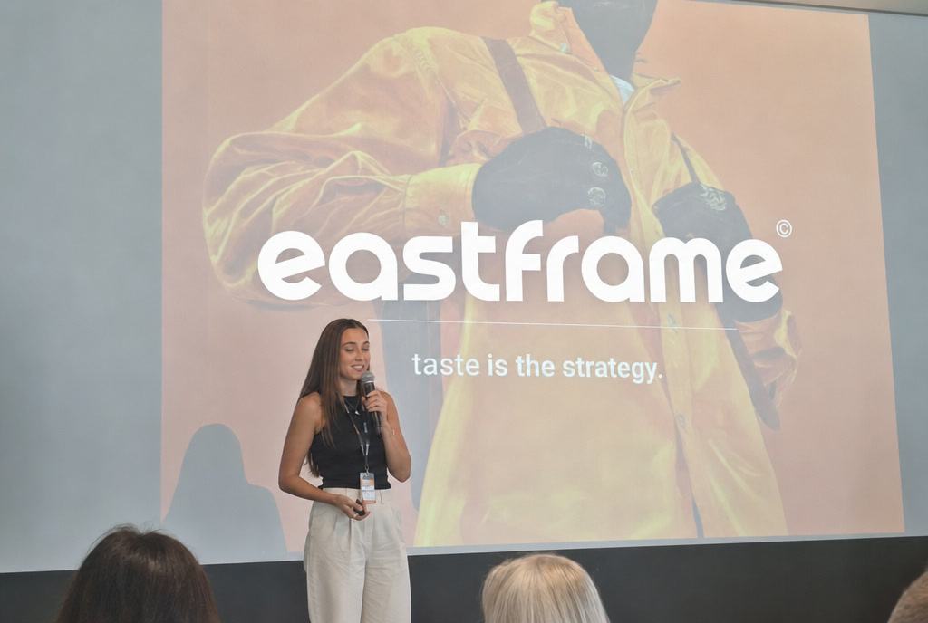 Kalbėtoja su mikrofonu stovi prieš ekraną, kuriame projektuojamas užrašas taste is the strategy.